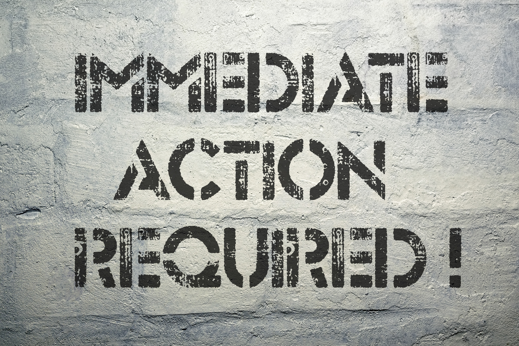 immediate action required exclamation stencil print on the grunge white brick wall